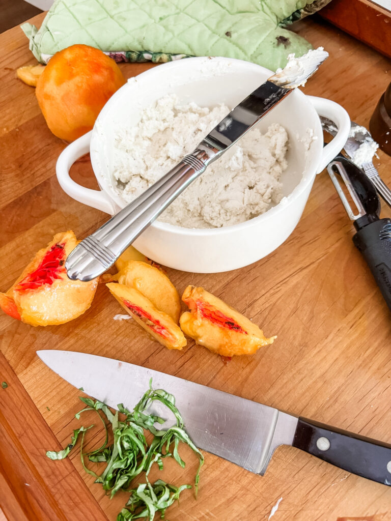 Ingredients for peach crostini including a baguette, fresh peaches, chèvre, olive oil, balsamic glaze, and fresh basil