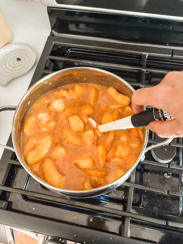 Peach pie filling simmering to a thick, glossy consistency in a large pot