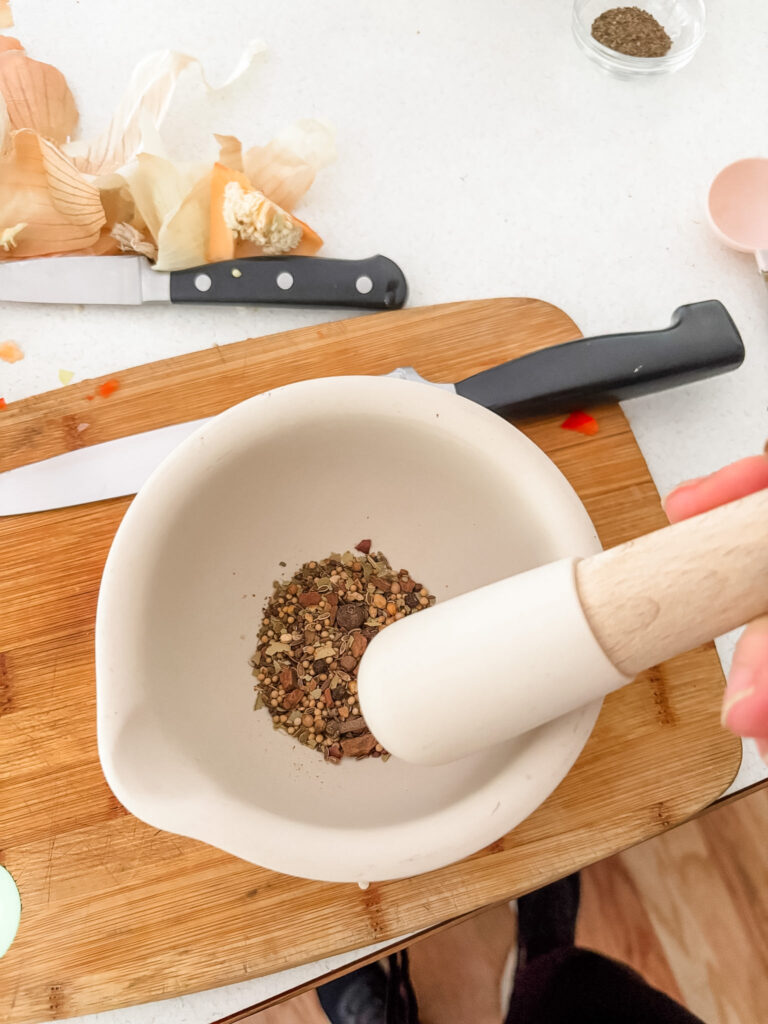 Pickling spices being lightly crushed with a mortar and pestle