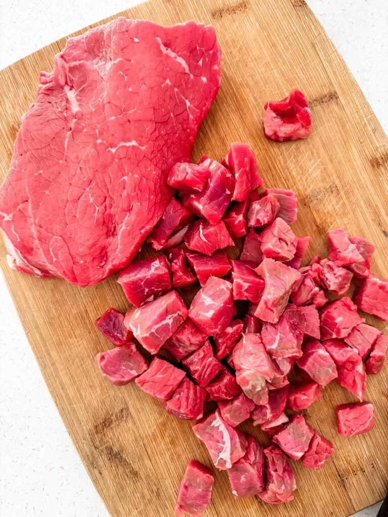 Lean beef sirloin trimmed of visible fat and cut into half-inch cubes on a wooden cutting board