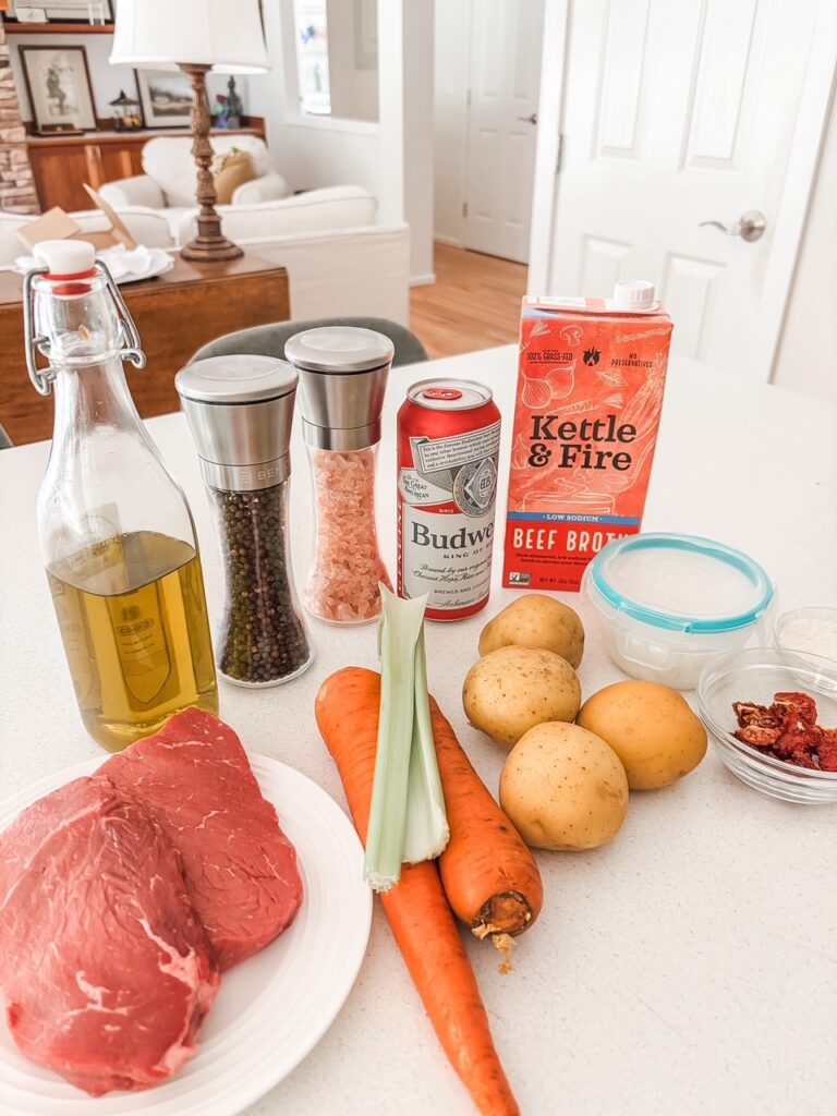 Ingredients for healthy beef and beer stew including lean beef sirloin, potatoes, carrots, celery, onion, sun-dried tomatoes, beer, and beef broth