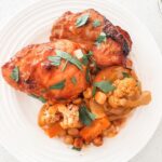 Mediterranean sheet pan dinner with chicken thighs, carrots, cauliflower, onion, and chickpeas in a smoky tomato rub