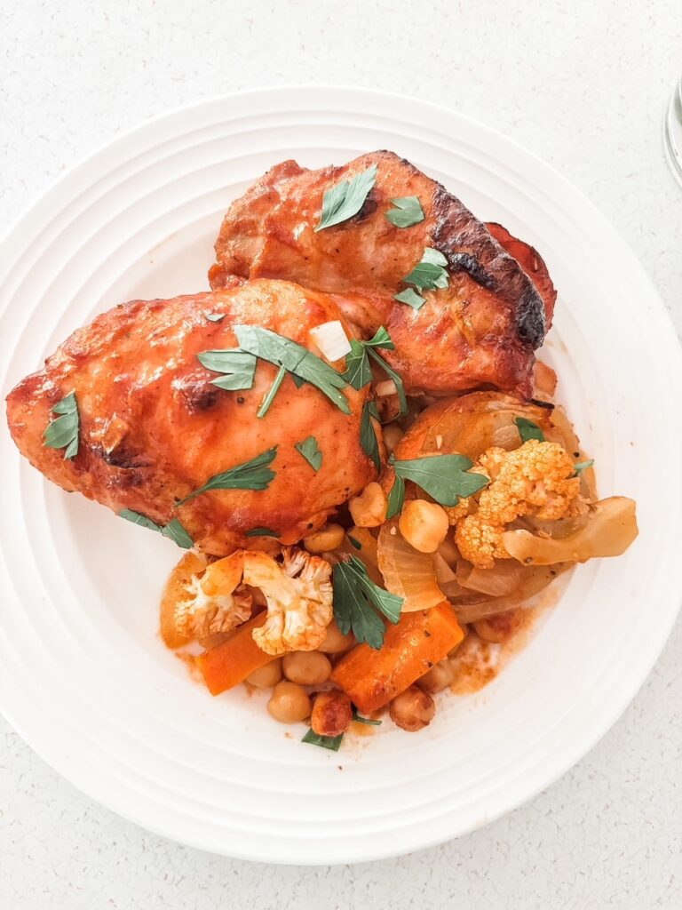 Mediterranean sheet pan dinner with chicken thighs, carrots, cauliflower, onion, and chickpeas in a smoky tomato rub
