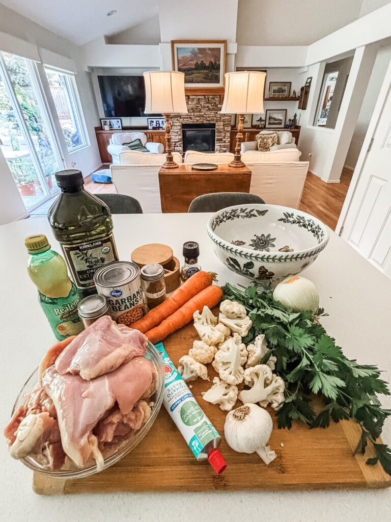 Ingredients for Mediterranean sheet pan dinner including chicken thighs, carrots, cauliflower, onion, chickpeas, garlic, lemon, tomato paste, cumin, and smoked paprika