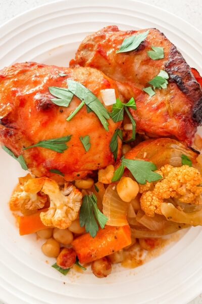Mediterranean sheet pan dinner with chicken thighs, carrots, cauliflower, onion, and chickpeas in a smoky tomato rub