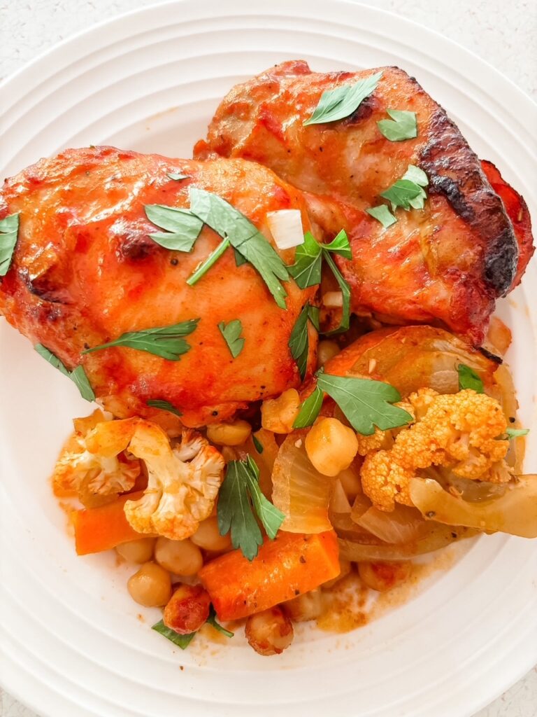 Mediterranean sheet pan dinner with chicken thighs, carrots, cauliflower, onion, and chickpeas in a smoky tomato rub